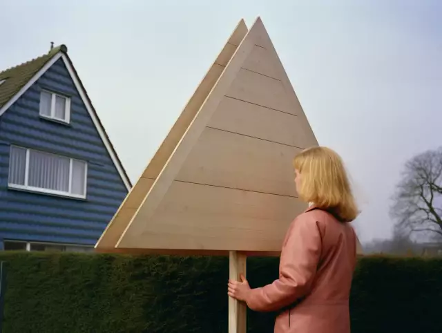 Ästhetische Intervention in deutscher Vorstadt, Kunststudentin trägt Holzschild vor einem Einfamilienhaus.