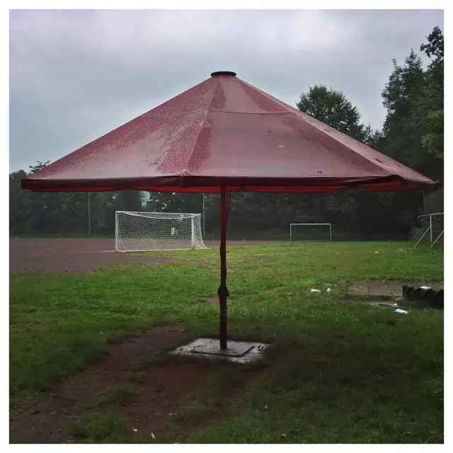 ein sehr gr0ßer Sonnenschirm im Regen auf einem Sportplatz