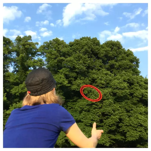 junge Frau mit Basecap wirf einen runden Frisbee-Ring vor einem Baum und blauen Himmel