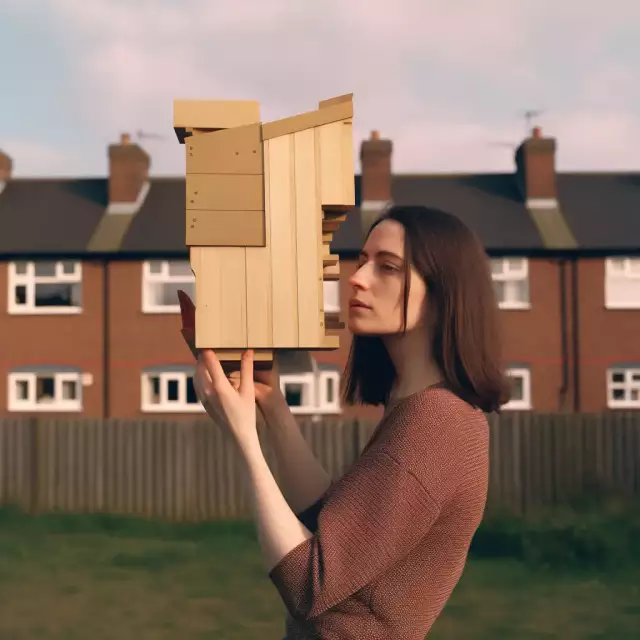 KI-generiertes Foto aus dem England der 1970er Jahre: Eine 30-jährige Architekturstudentin präsentiert ihr hölzernes Architekturmodell.
