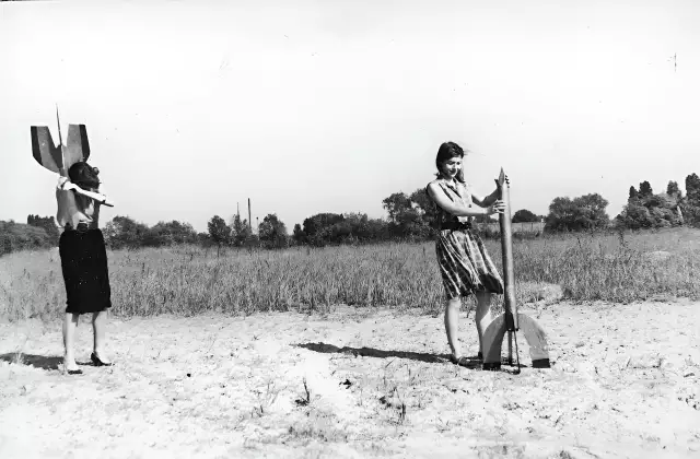Zwei junge Frauen - Raketenmädchen - hantieren mit Holzraketen. Die schwarz-weiße Aufnahme zeigt sie in einer dynamischen Pose.