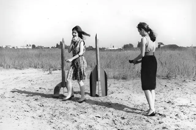 Zwei junge Frauen - Raketenmädchen - hantieren mit Holzraketen. Die schwarz-weiße Aufnahme zeigt sie in einer dynamischen Pose.Die Raktenen werden - wie für einen Start - aufgebaut.